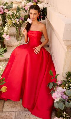 A person wearing a red Ava Presley 47374 minimalist prom dress sits on stone steps surrounded by flower arrangements.