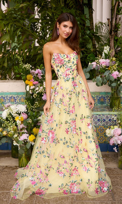 Woman wearing a strapless, floor-length Ava Presley 47391 yellow prom dress with floral embroidery, standing in front of flower arrangements.