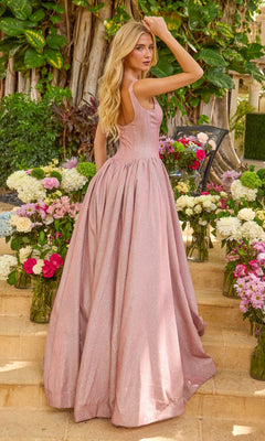 A person wears the Ava Presley 47400, a dusty pink, shimmery, floor-length corset prom dress with a square neckline and a full skirt, standing amidst vases of flowers.