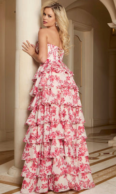 A woman in the Jovani 47404 Long Prom Dress—strapless, floor-length with pink and white floral ruffles—stands indoors, leaning against a column and glancing over her shoulder.