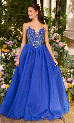 A woman wearing a royal blue Ava Presley 47430 ball gown with a beaded, plunging neckline and a full tulle skirt, standing in front of floral arrangements.