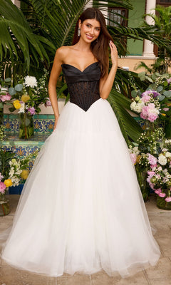 A woman wears an Ava Presley 47484 strapless corset ball gown with a black bodice and a full white tulle skirt, standing in front of floral arrangements.