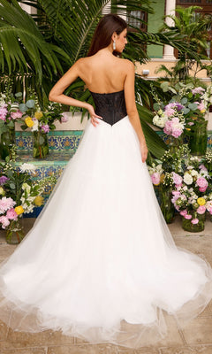 A woman wears an Ava Presley 47484 strapless corset ball gown with a black bodice and full white tulle skirt, standing in front of floral arrangements.