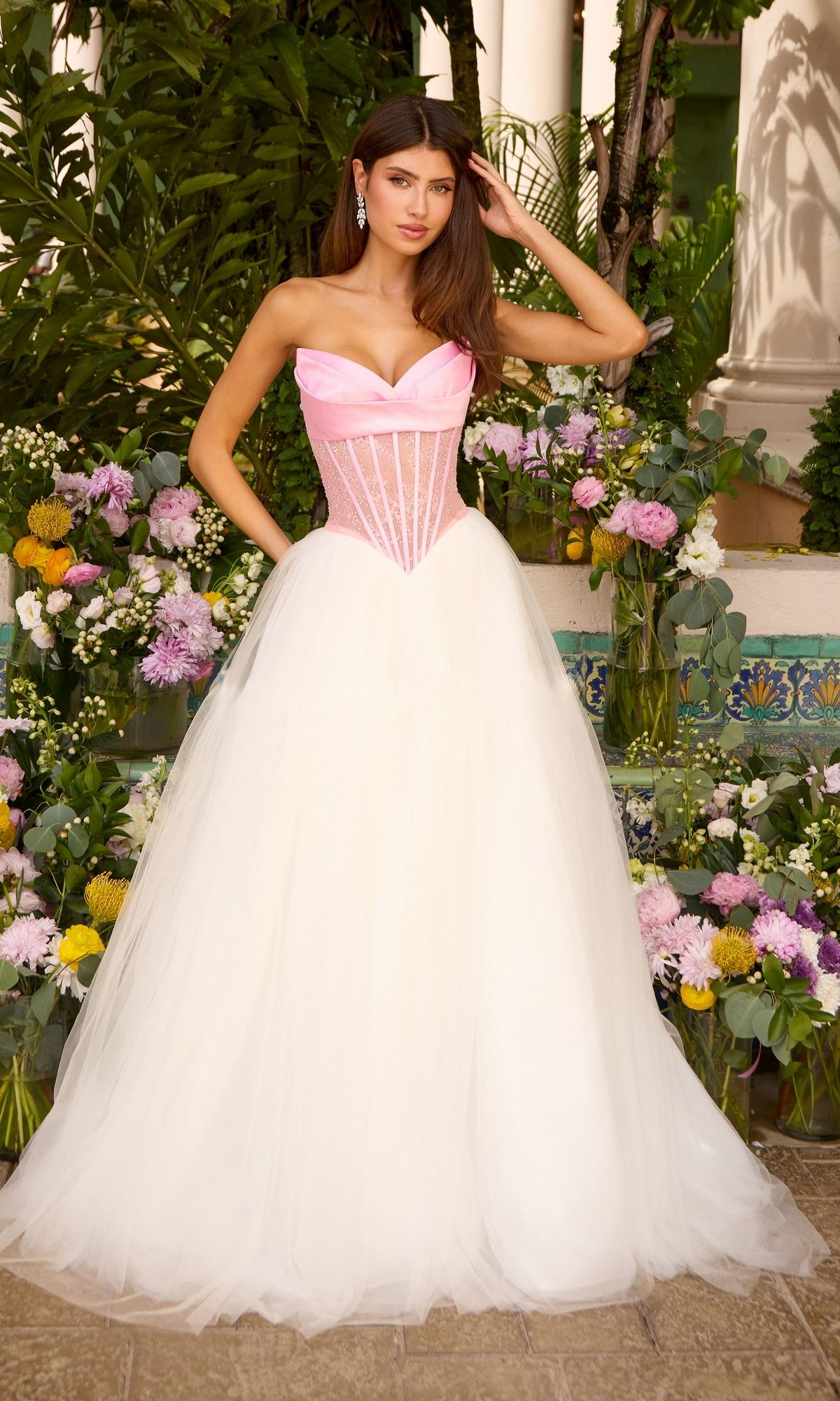 Long Prom Dress: Ava Presley 47484 strapless corset ball gown with a pink bodice, exposed boning, and a voluminous white tulle skirt standing among floral arrangements.