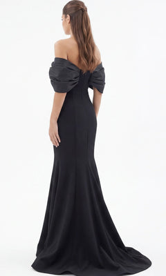 A woman stands facing away against a plain white background, wearing the Jovani 47657 long formal dress—an off-the-shoulder, floor-length black gown with puffed sleeves.