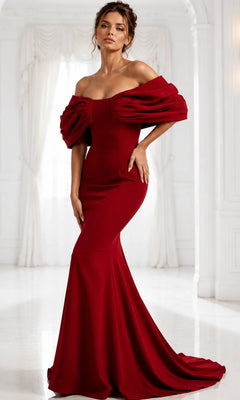 A woman is seen standing in an elegant white room, wearing the Long Formal Dress: Jovani 47657—an exquisite, floor-length designer gown featuring an off-the-shoulder neckline and dramatic sleeves.