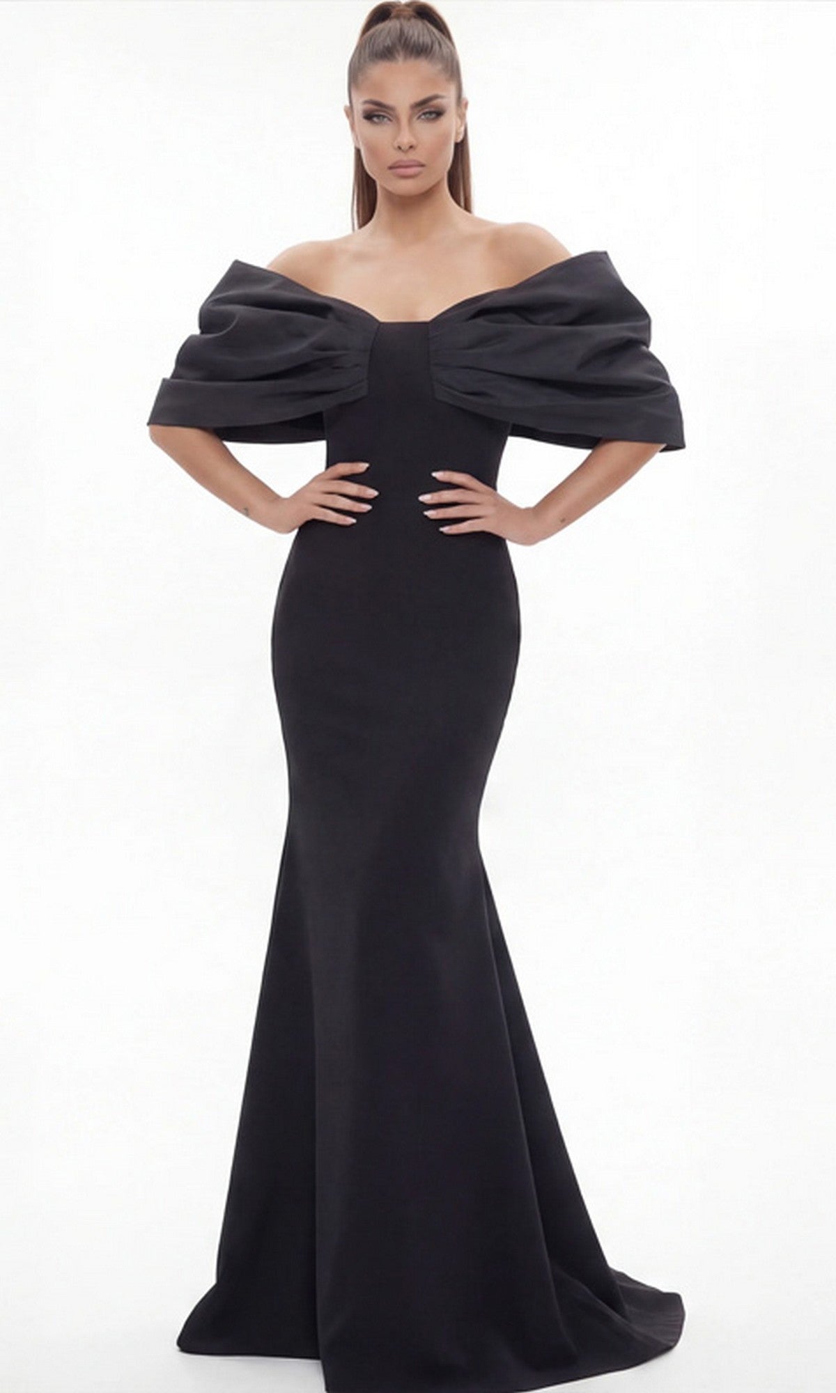 A woman wearing the Long Formal Dress: Jovani 47657—a fitted, black, off-the-shoulder gown with voluminous sleeves—stands against a plain white background, channeling sophisticated elegance.