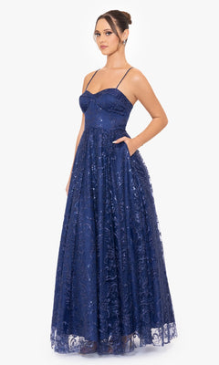 A woman stands against a white background wearing the Blondie Nites 4768BN long navy formal dress, featuring thin straps, sequin details, an embroidered overlay, and an elegant A-line silhouette.