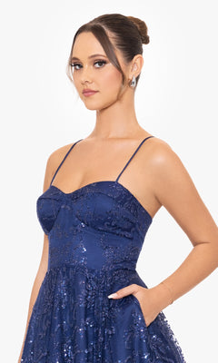 A woman with her hair in a bun models the Blondie Nites 4768BN, a sleeveless long navy formal dress featuring sequins, thin straps, and pockets, standing against a plain white background.