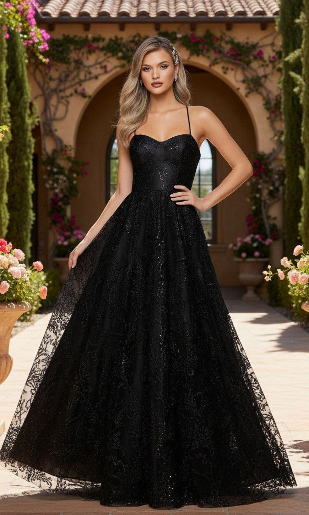 A woman in the Blondie Nites 4768BN long navy formal dress with thin straps stands outdoors before an arched doorway, surrounded by flowers and greenery.