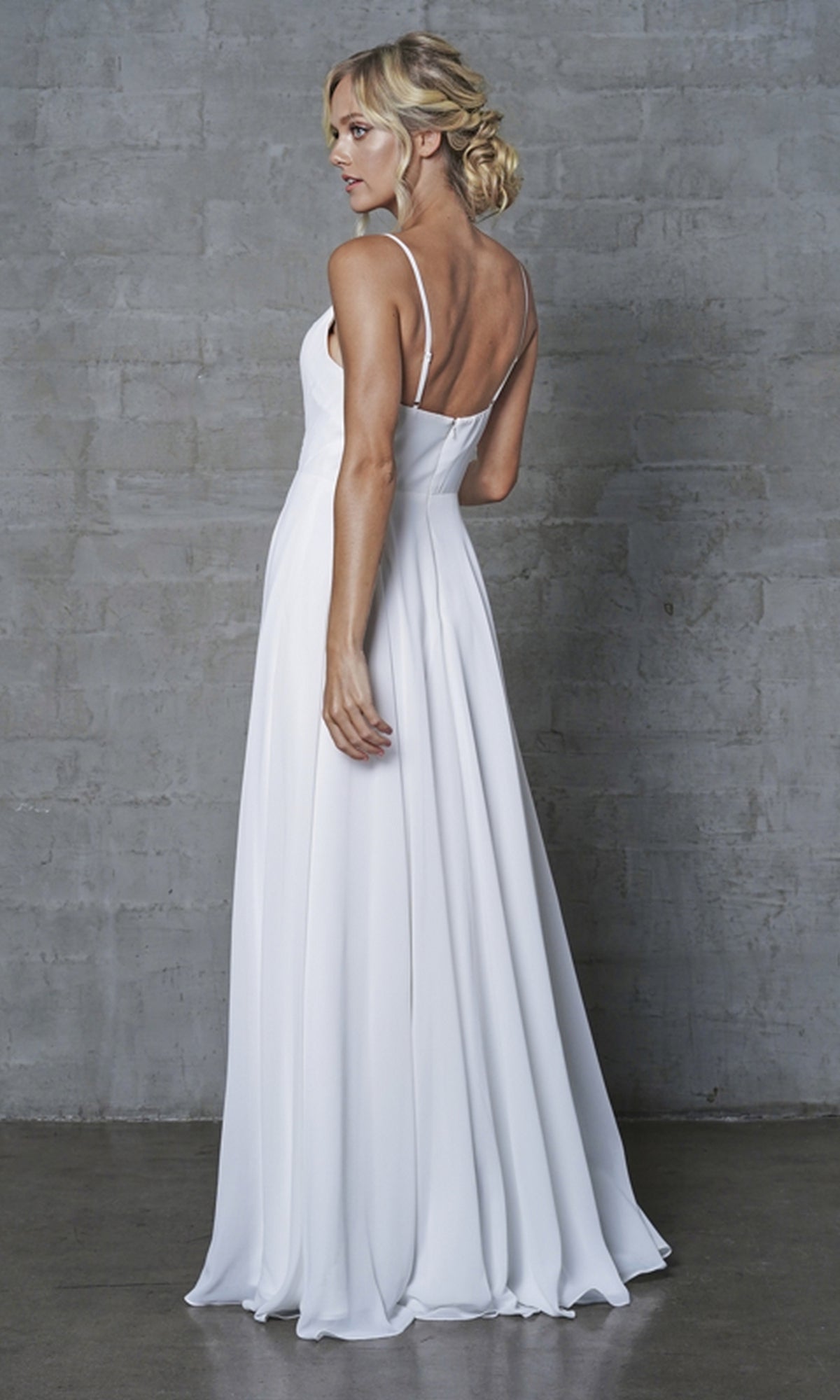 A woman with blonde hair in an updo wears the Simple V-Neck Long A-Line Prom Dress 477, standing sideways and looking over her shoulder against a gray textured wall.