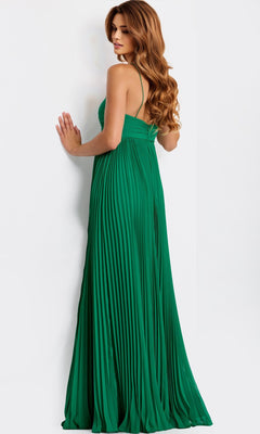 A woman with long, wavy hair stands facing a white wall and looks over her shoulder, wearing the floor-length green Jovani 47820 prom dress with pleats.