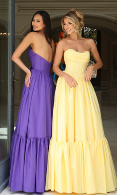 Two women stand indoors, smiling and looking over their shoulders. One wears the Jovani 47883 Strapless Long Ruffled Prom Dress with a corset-style bodice, while the other is in a yellow prom dress.