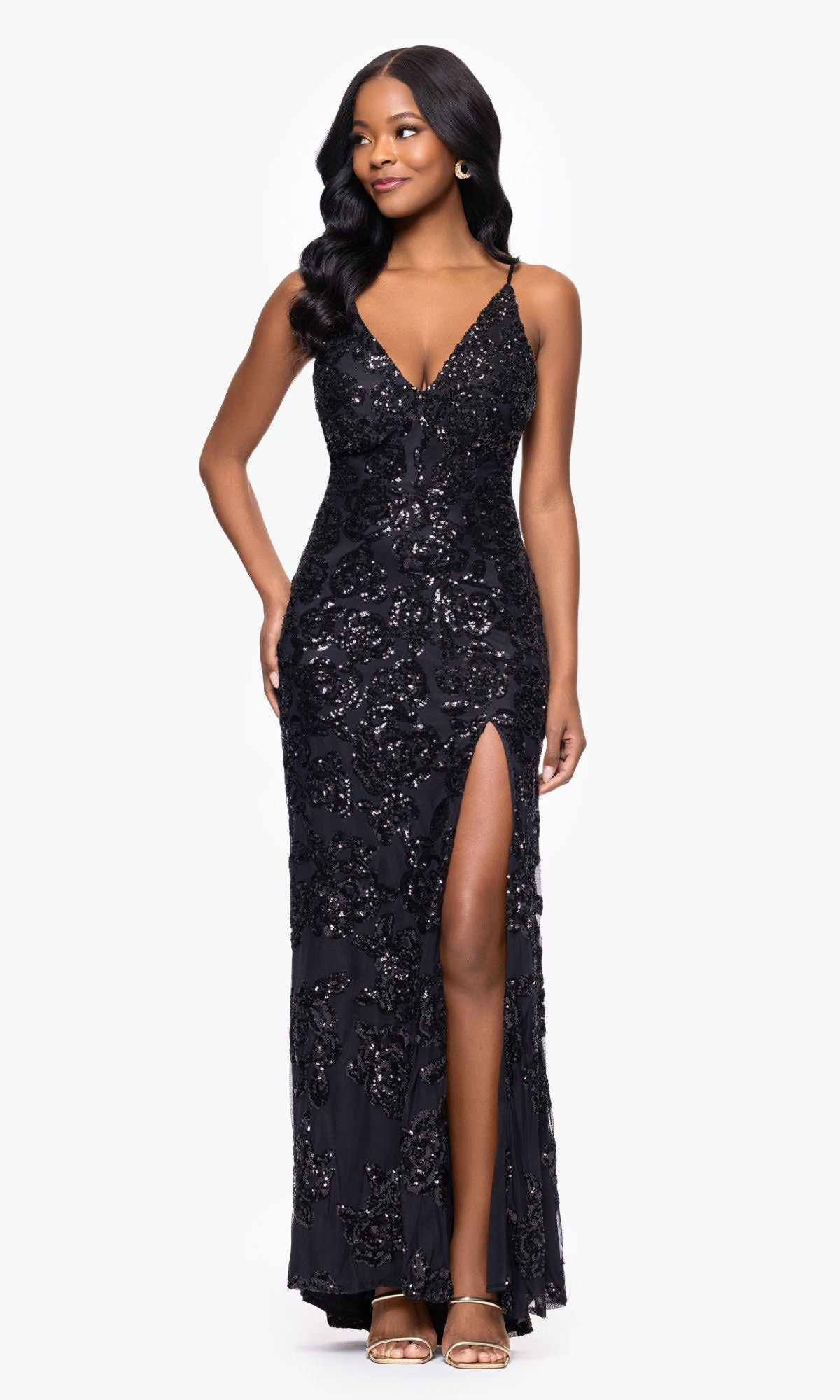A woman models the Long Black Sequin Prom Dress: Blondie Nites 4817BN—a sleeveless gown with a deep V-neck, thigh-high slit, and open-toe heels—posing against a plain white background.