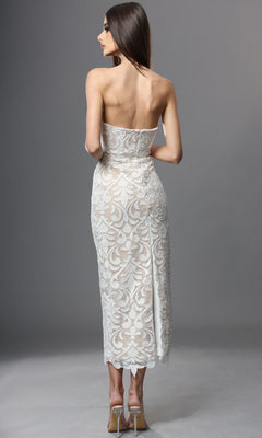 A woman is seen from behind, standing on a gray background, wearing the Jovani 48461 Midi Semi-Formal Dress—a strapless design with white lace overlay and nude lining.