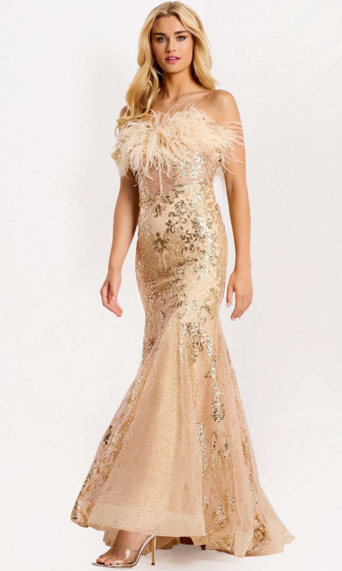 A woman models the Jovani 48465 Long Prom Dress in gold, featuring a floor-length mermaid silhouette, off-the-shoulder feathered neckline, and sheer overlay, standing against a plain white background.