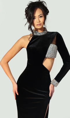 A woman poses against a plain light background wearing the Long Prom Dress: Jovani 48481, a black gown with an asymmetrical design, one long sleeve, silver embellishments, and a side cutout.