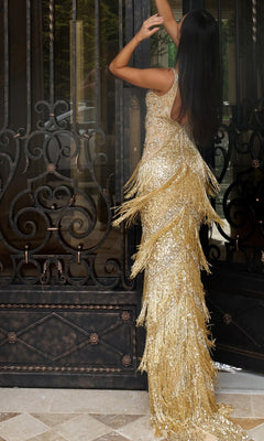 A woman wearing the Jovani 48521 long prom dress with a shimmering sequined beaded bodice stands with her back to the camera, raising her arms in front of ornate black metal doors.