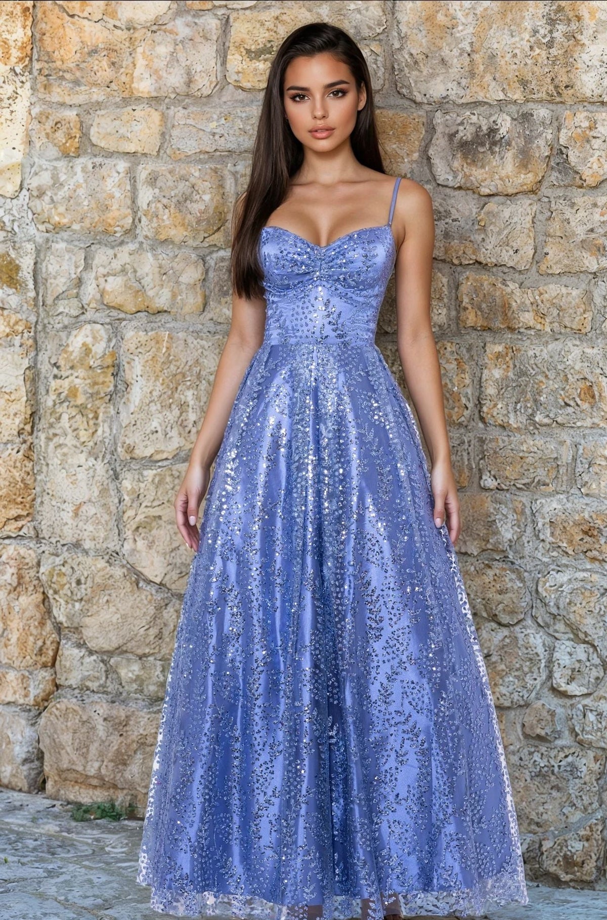 A woman in a budget-friendly, sleeveless periwinkle Long Glitter Prom Dress (Blondie Nites 4867BN) stands before a stone wall.