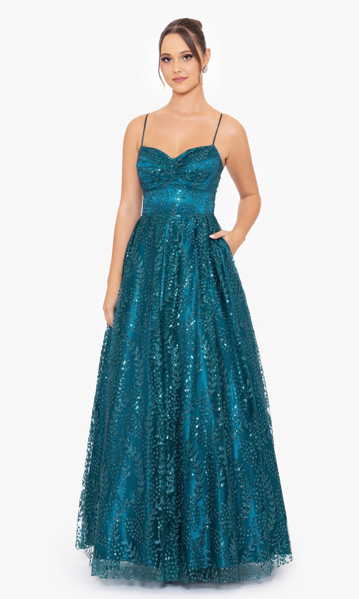 A woman stands against a plain white background wearing the Blondie Nites 4867BN Long Glitter Prom Dress, an affordable teal, floor-length gown with sequins, thin straps, and a sweetheart neckline.