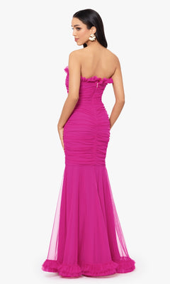 A woman stands facing away, showcasing the fitted mermaid silhouette of the Hot Pink Strapless Long Prom Dress 4868BN, a floor-length gown with ruffle details by Blondie Nites.