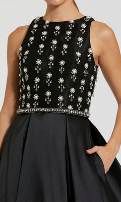 Woman in the Mac Duggal 48803 long formal dress with a sleeveless embellished bodice, satin A-line skirt, and one hand in the pocket.