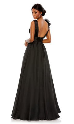 A woman stands facing away, looking over her shoulder in the Mac Duggal 48856 Ruffled Long Prom Ball Gown—a floor-length, sleeveless black dress with an open back—against a plain white background.