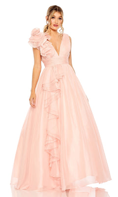 A woman wears the Mac Duggal 48856 Ruffled Long Prom Ball Gown, a floor-length light pink dress with a deep V-neck, ruffled details, and a large floral accent on one shoulder.