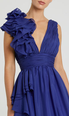 Woman wearing the Mac Duggal 48856 Ruffled Long Prom Ball Gown, a sleeveless deep blue dress featuring a deep V-neckline and layered ruffle detail on one shoulder.