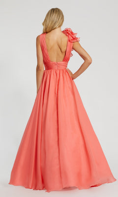 A woman stands with her back to the camera in the Mac Duggal 48856 Ruffled Long Prom Ball Gown, a sleeveless, floor-length coral dress featuring a deep V-back and ruffled detail on one shoulder.
