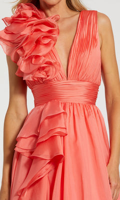 A woman in the Mac Duggal 48856 Ruffled Long Prom Ball Gown features a sleeveless coral design with a deep V-neck, pleated bodice, fitted waistband, and large ruffled accents on the shoulder and skirt.