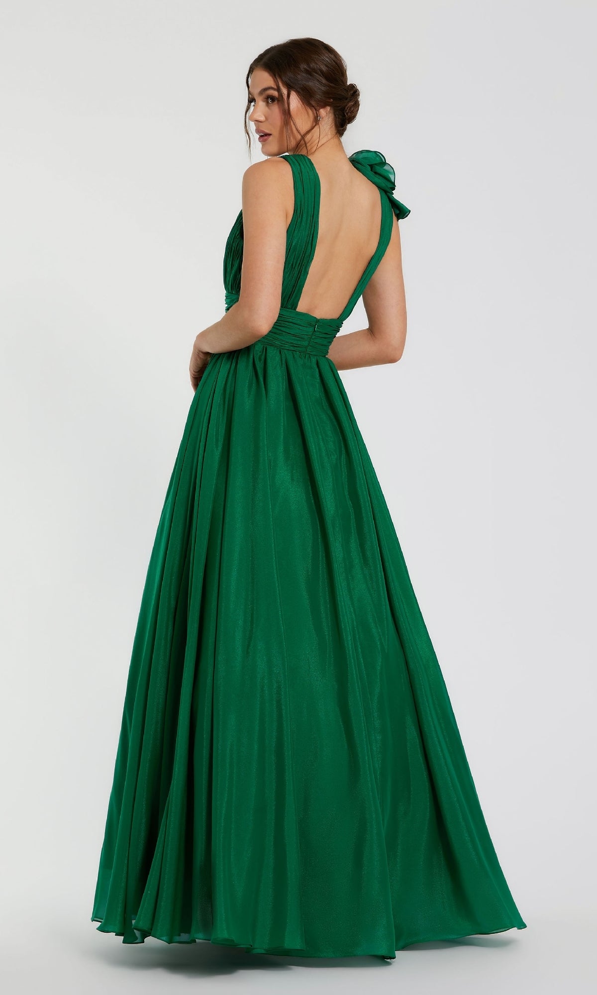 A woman stands facing away, looking over her shoulder in the Mac Duggal 48856 Ruffled Long Prom Ball Gown—an emerald green, floor-length, sleeveless dress with an open back.