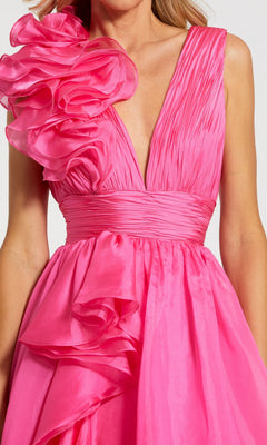 A woman wearing the Mac Duggal 48856 Ruffled Long Prom Ball Gown—a sleeveless, bright pink A-line dress with a deep V-neck and bold ruffled details on the left shoulder and waist.