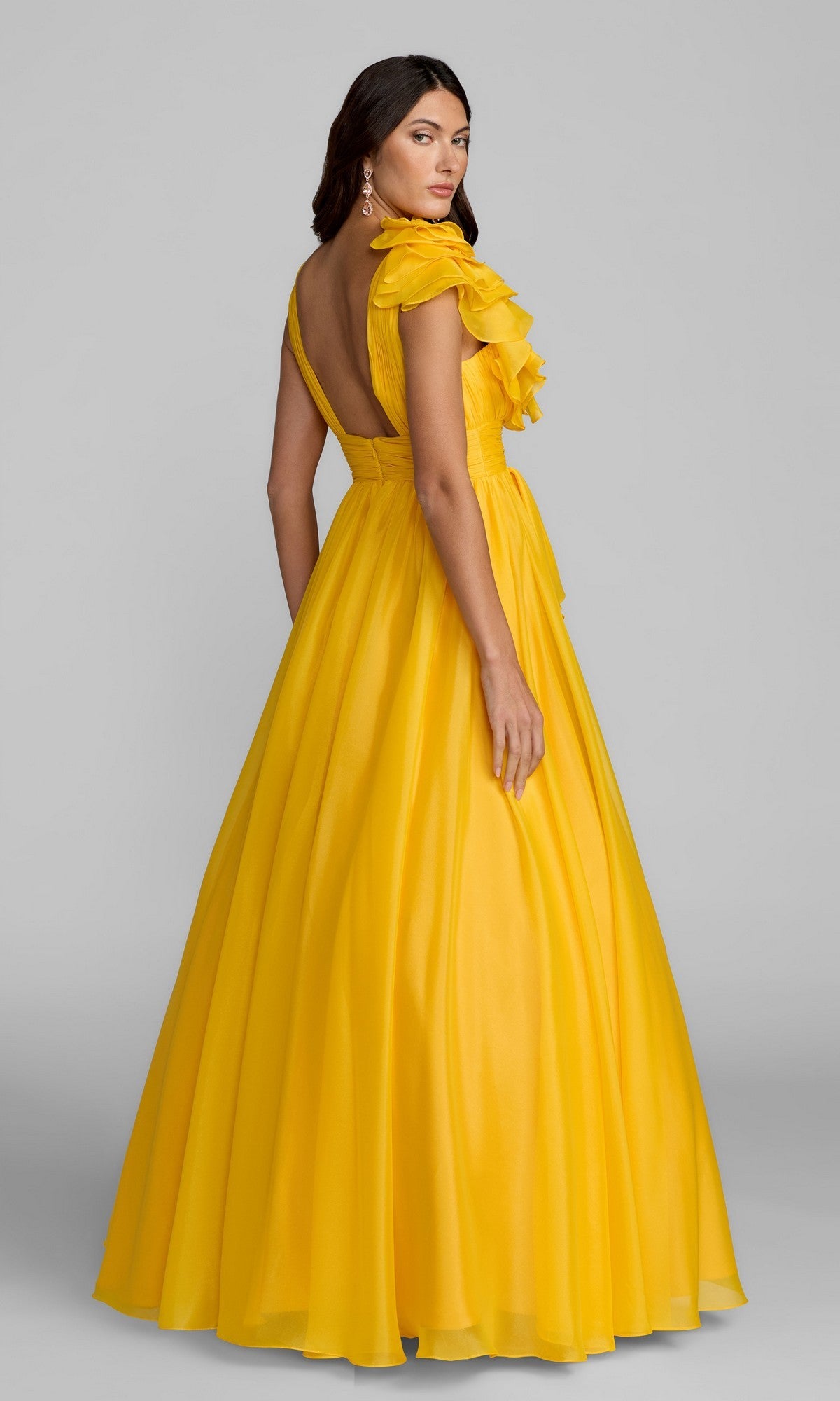 A woman models the Mac Duggal 48856 Ruffled Long Prom Ball Gown, a yellow, floor-length, one-shoulder dress with ruffle details, standing against a plain gray background.