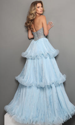 A woman in the Long Formal Dress: Jovani 48948, a strapless ball gown with a crystal embellished bodice, stands facing a gray wall and looks over her shoulder. The ruffled blue pageant dress shimmers elegantly, capturing the light with every delicate fold.