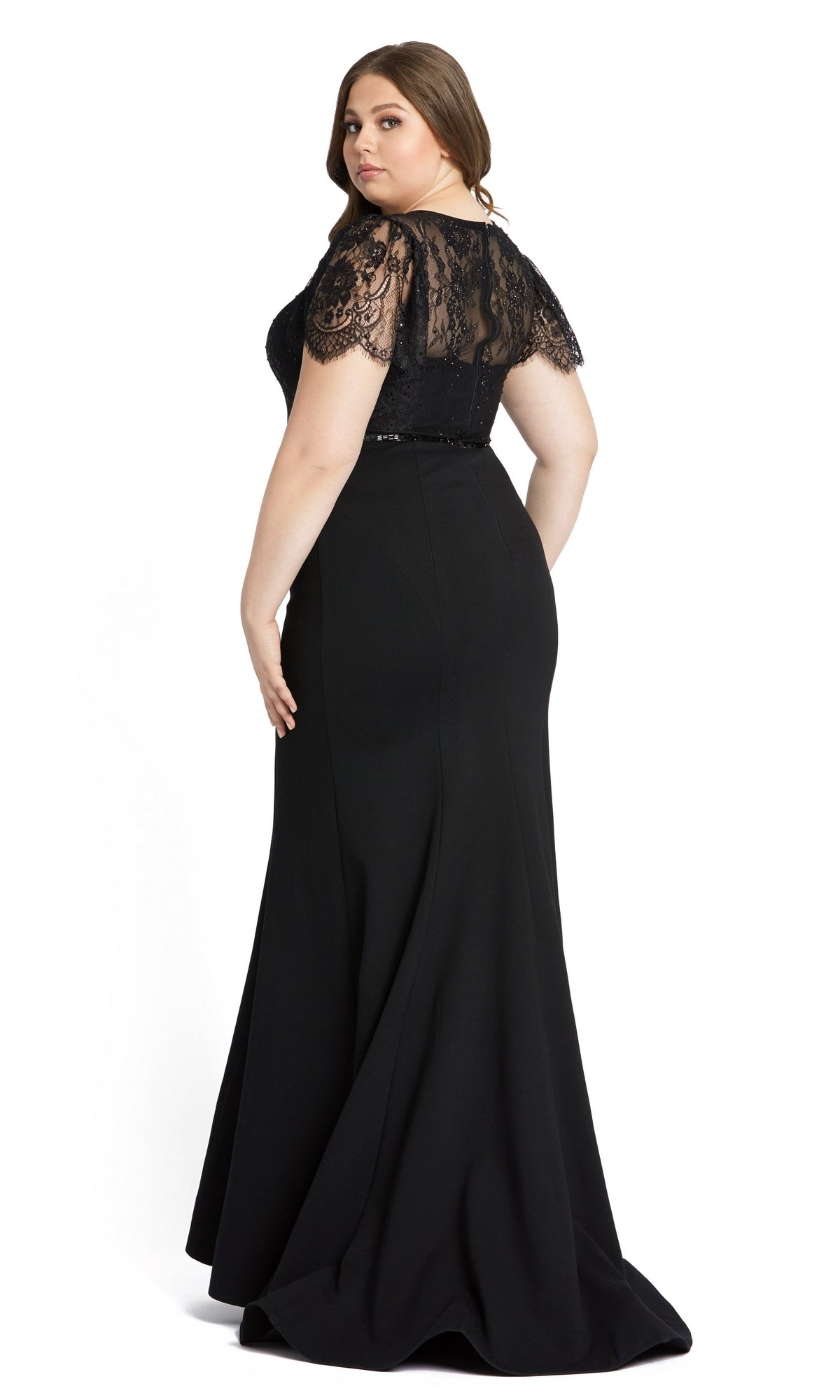 A woman models the Long Plus-Size Formal Dress 48984 by Mac Duggal, a black floor-length mermaid gown with lace flutter sleeves, standing and looking over her shoulder against a plain white background.