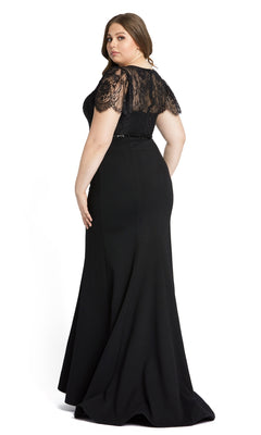 A woman models the Long Plus-Size Formal Dress 48984 by Mac Duggal, a black floor-length mermaid gown with lace flutter sleeves, standing and looking over her shoulder against a plain white background.