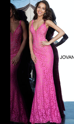 A woman in the Jovani 48994 Illusion-Sides Long Lace Prom Dress stands smiling in front of a reflective glass wall, showcasing the fitted, floor-length bright pink gown with rhinestone details.