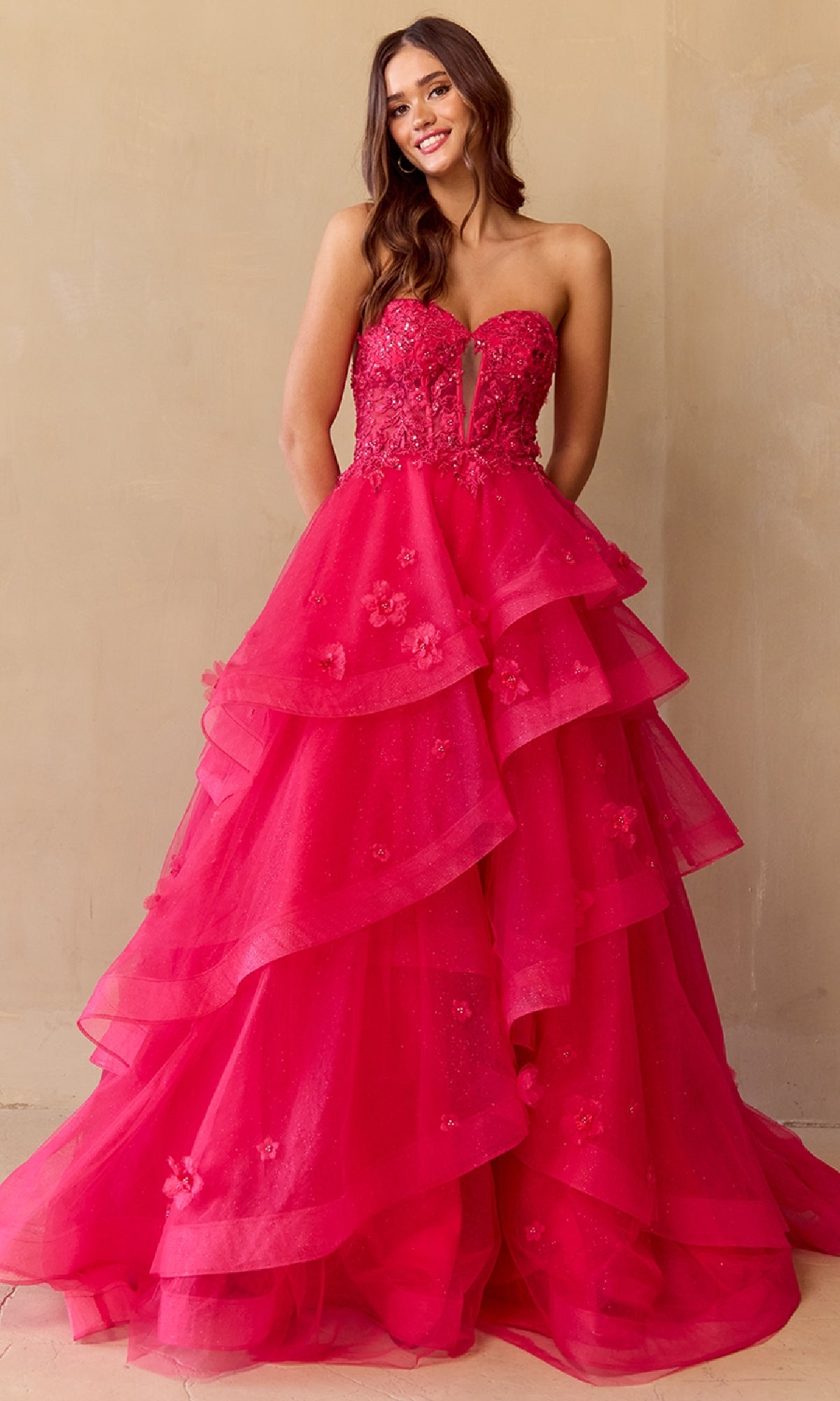 Woman wearing a hot pink strapless ball gown with ruffled layers on a beige background