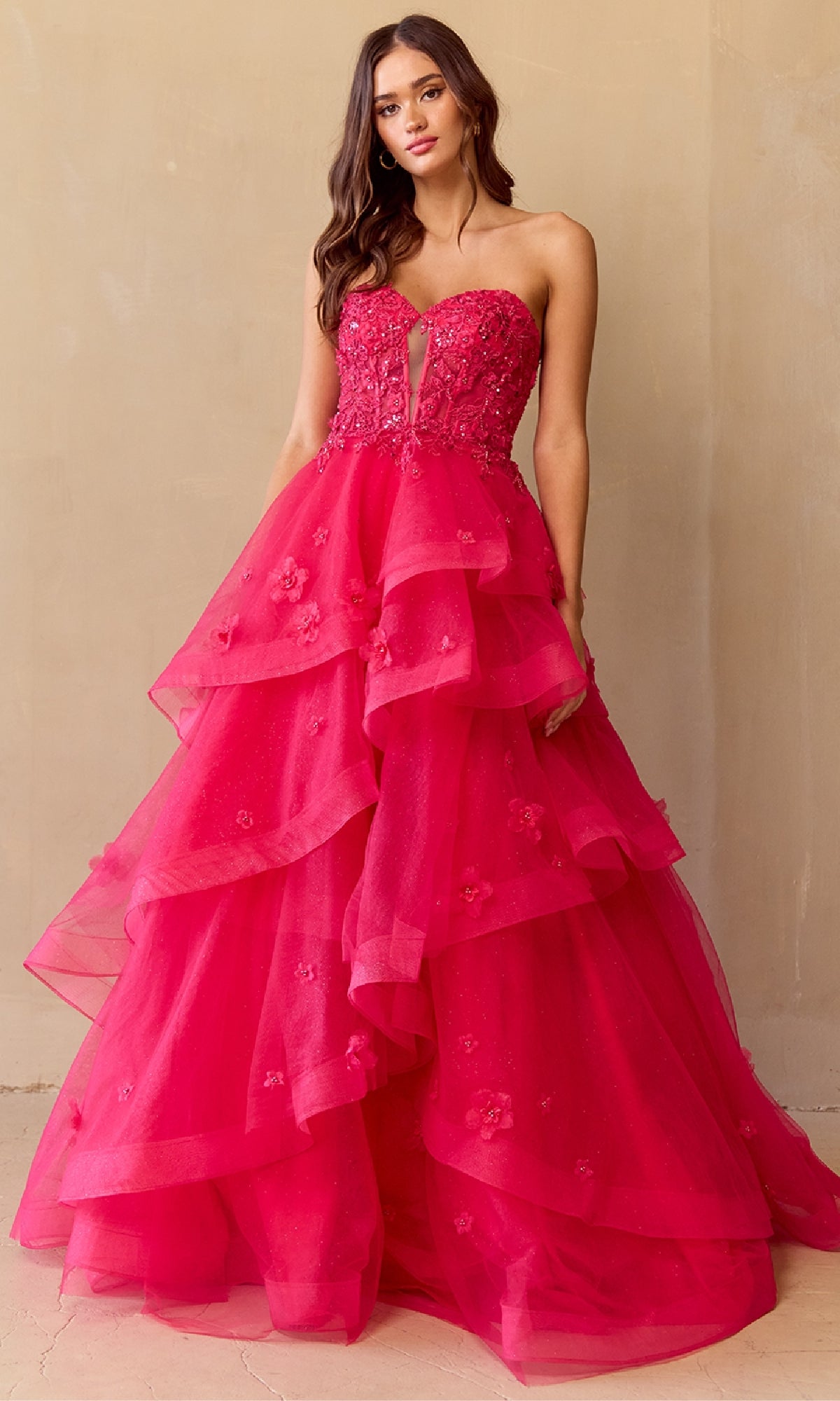 Woman wearing a hot pink strapless ball gown with ruffled layers on a beige background