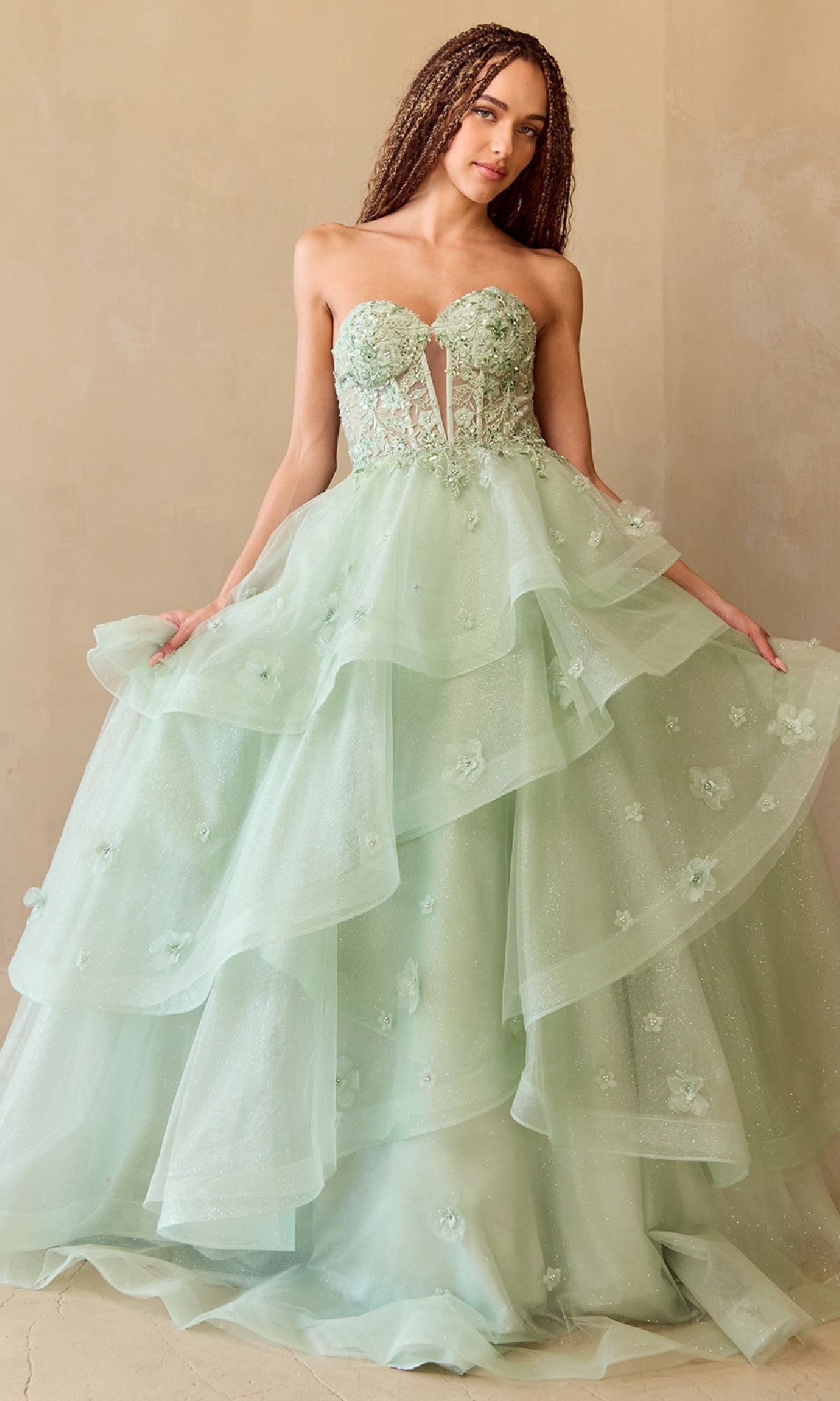Woman wearing a light green strapless ball gown with floral details and a layered tulle skirt on a beige background