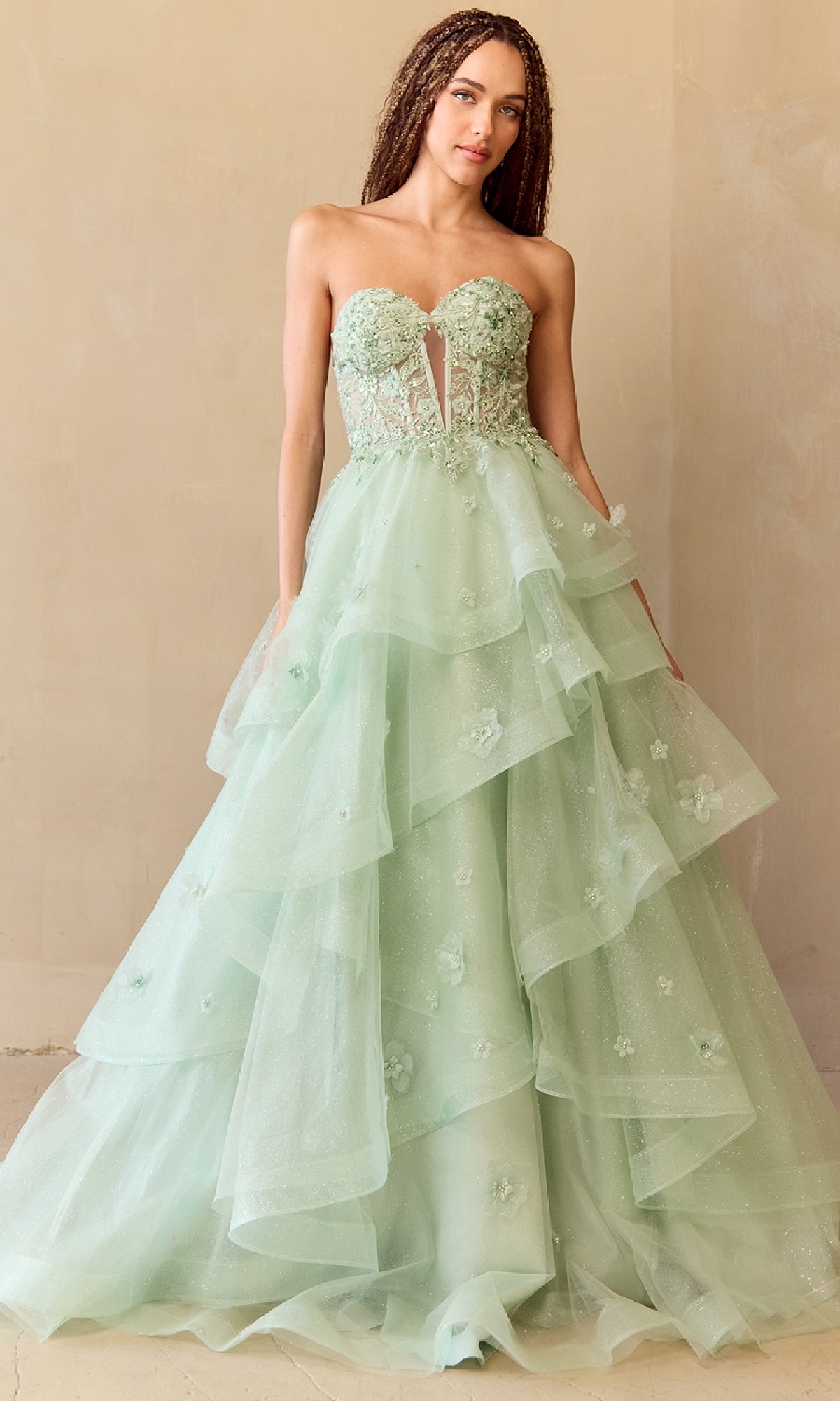 Woman wearing a light green strapless ball gown with floral details against a beige background