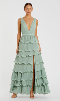 A woman models the Mac Duggal 49054 V-Neck Long Ruffle Prom Gown—a sleeveless, pale green A-line dress with a deep V-neck and high front slit—against a plain white background.