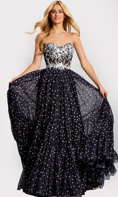 A woman wearing the black Jovani 49086 long prom dress, featuring a strapless floral lace corset bodice and a full, flowing A-line skirt with scattered white polka dots.