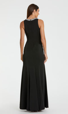 A woman stands facing away against a plain white background, wearing the Mac Duggal 49093 Beaded-Neck Long Prom Dress—a sleeveless gown with a fitted waist and silver beaded embellishments on the collar.