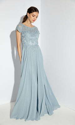 A woman stands against a white background wearing the Eureka 4909, a light blue short-sleeve long A-line formal dress with an embroidered lace bodice and flowing chiffon skirt, styled elegantly for dance.