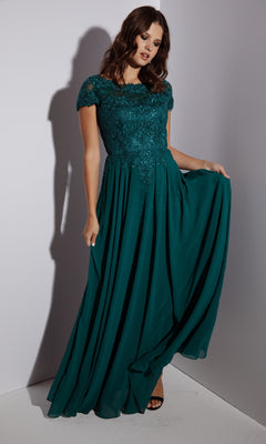 Woman in the Eureka 4909 Short-Sleeve Long A-Line Formal Dress, featuring an embroidered lace bodice and flowing chiffon skirt, stands against a plain background while holding the edge of her gown.