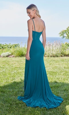 A woman stands on grass facing away, wearing the Long Prom Dress: Morilee 49127—a teal, floor-length gown with a lace bodice—set against a scenic outdoor backdrop with the ocean in the distance.