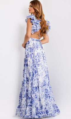 A woman stands sideways in the Jovani 49143 Ruffled Long Print Prom Dress, featuring white and blue florals, ruffled sleeves, and an open back, against a plain white background.