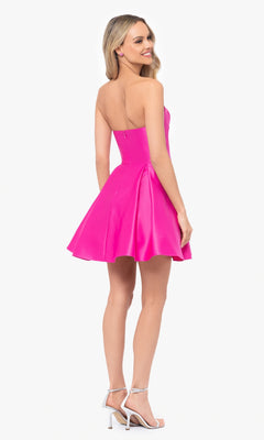 A woman with long blonde hair wears the Short Strapless Sweetheart Hoco Dress 4914BN in bright pink, featuring a ruched waist, paired with silver high-heeled sandals. She stands smiling over her shoulder.